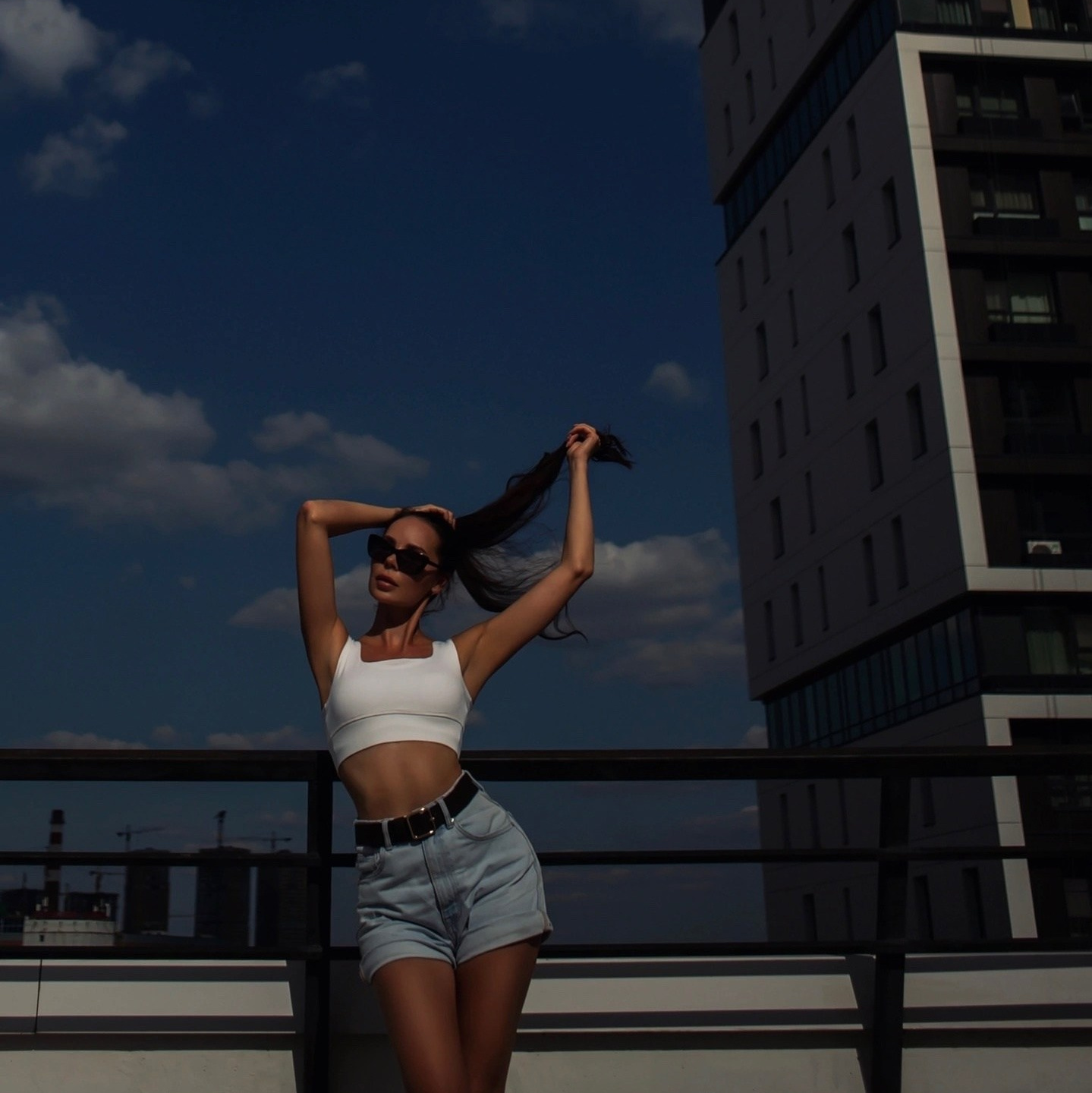 Девушка в топе и шортах стоит на крыше