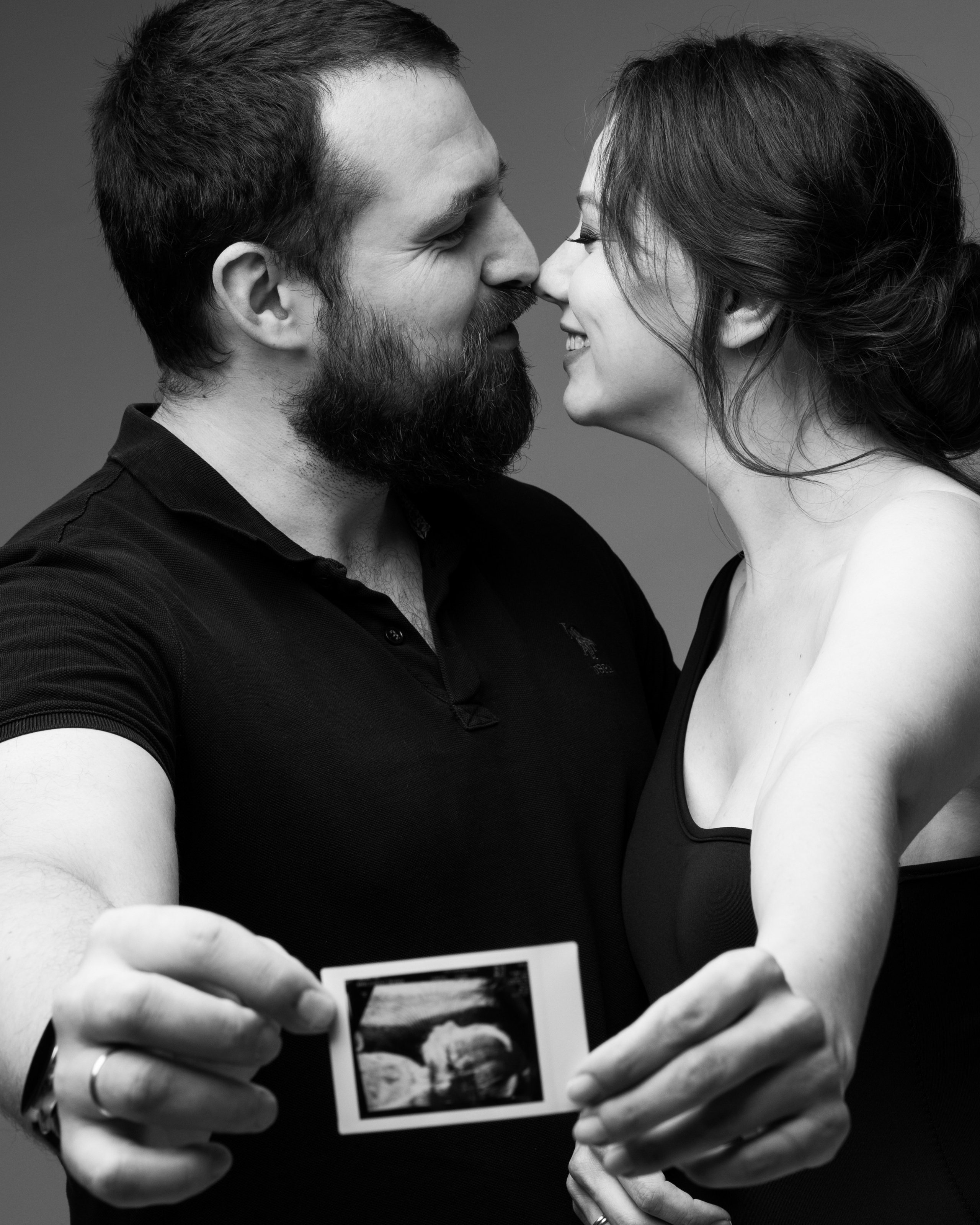 Мужчина и женщина на черное-белой фотографии держат снимок УЗИ беременности и искренне улыбаются друг другу