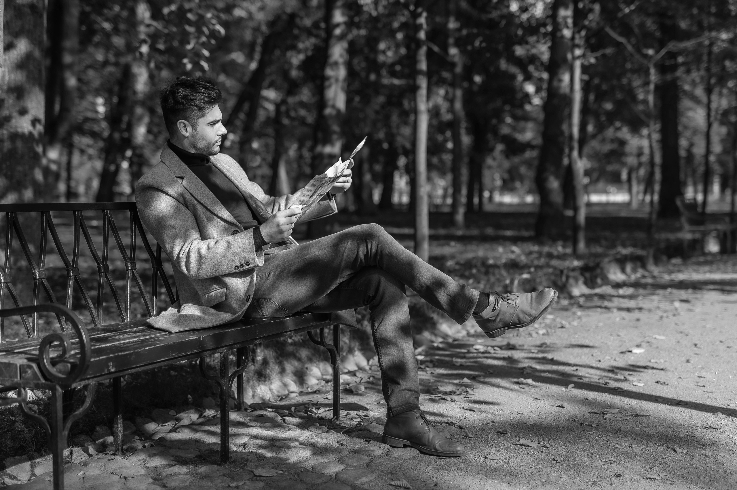 Молодой джентльмен на кованной скамье в парке читает прессу