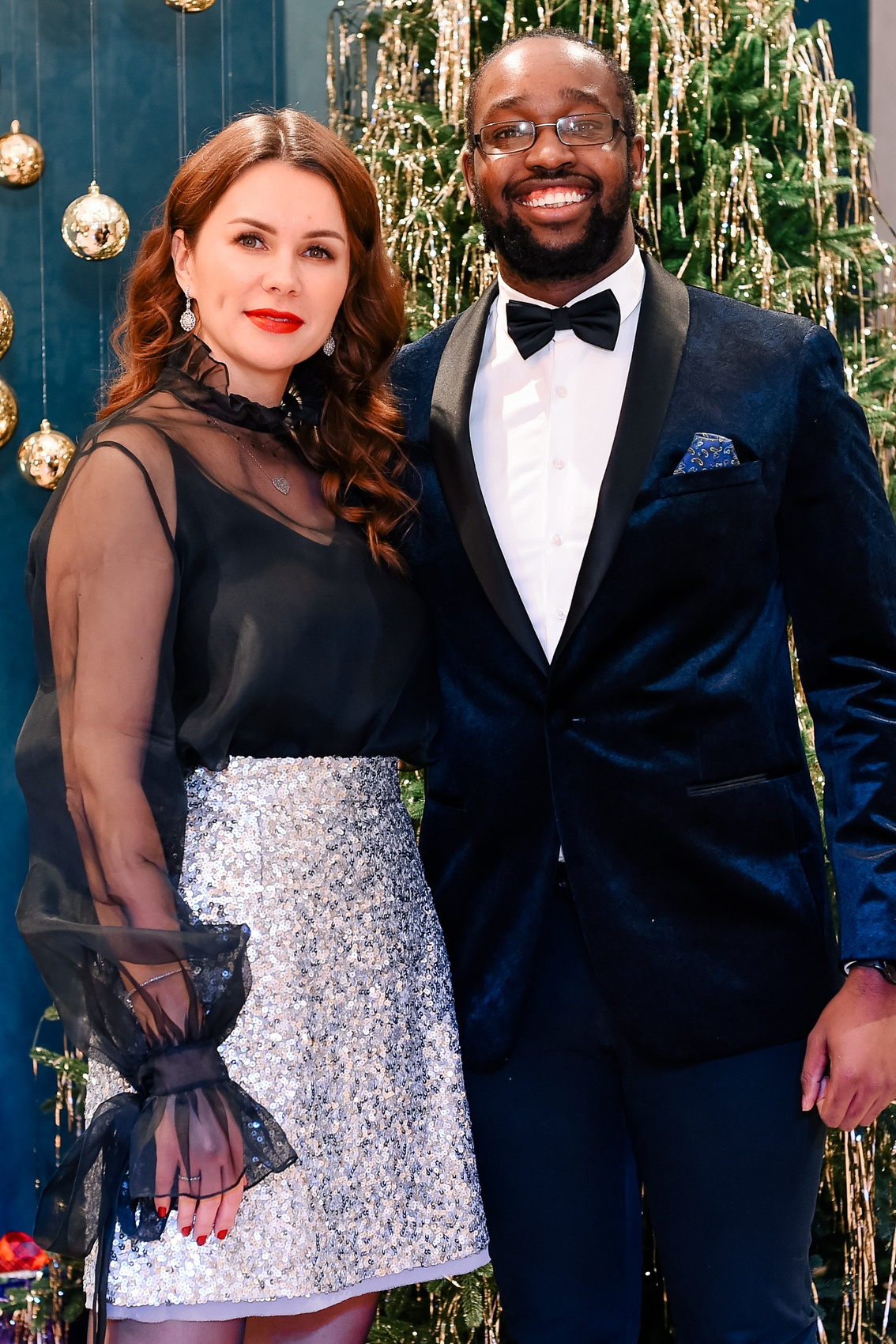 Девушка и молодой человек - афроамериканец стоят на фоне новогодней елки, обнявшись