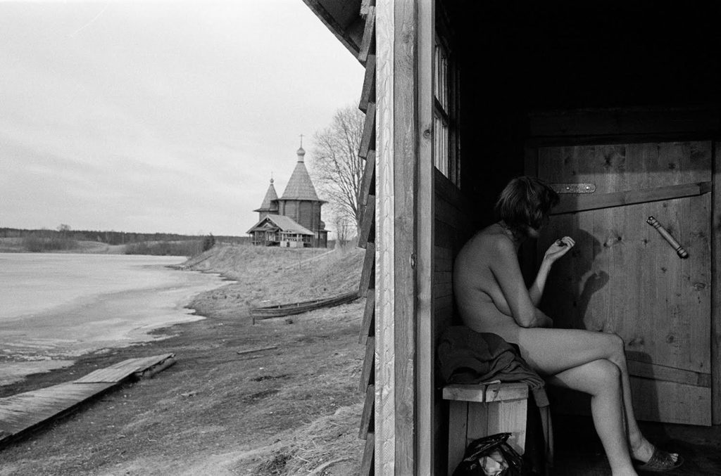 Tatiana sitting in a bathhouse with a view of the Church of the Nativity of the Virgin in Kolodozero. August 2014.