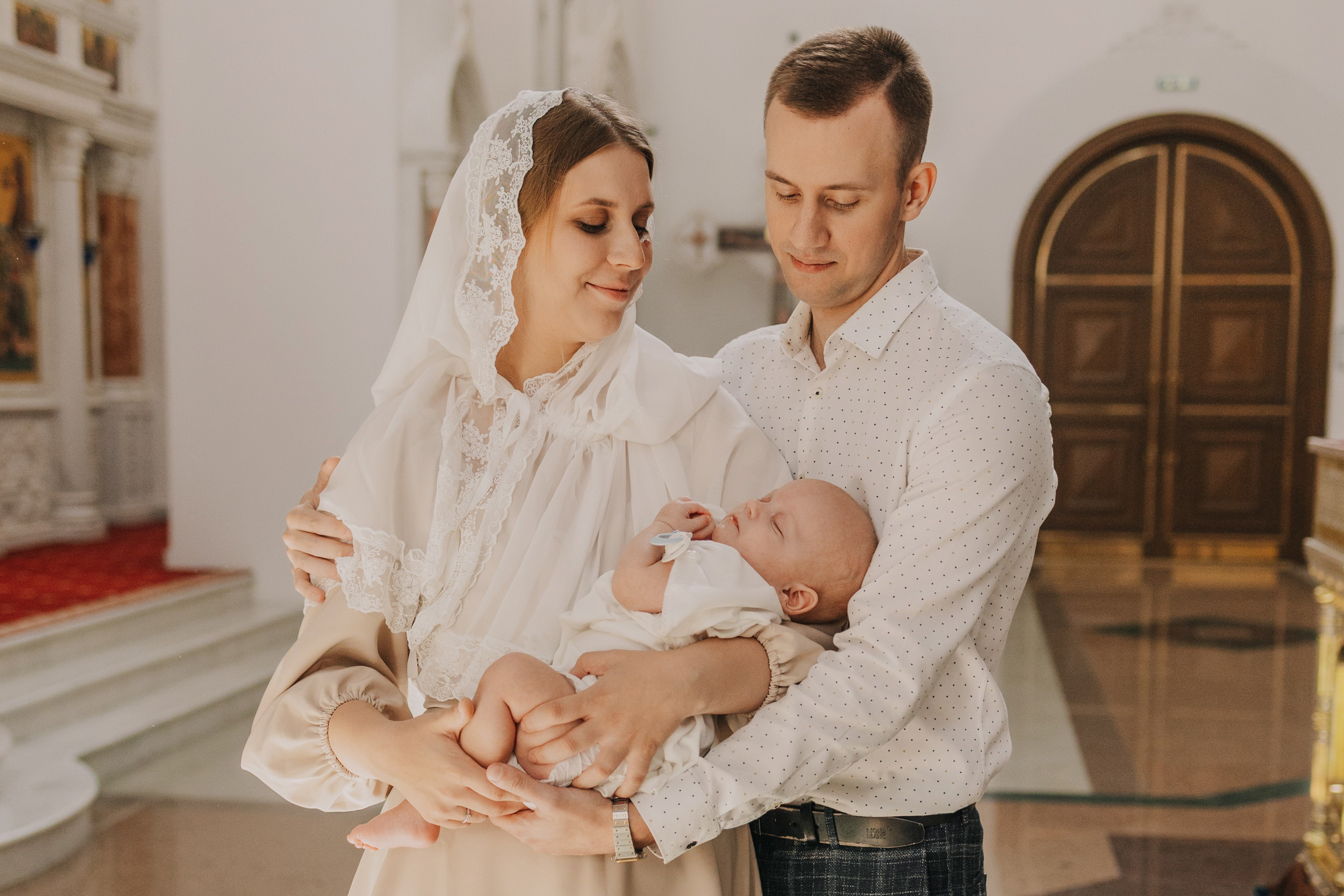 Фотограф на крещение в храме, родители держат своего ребенка.