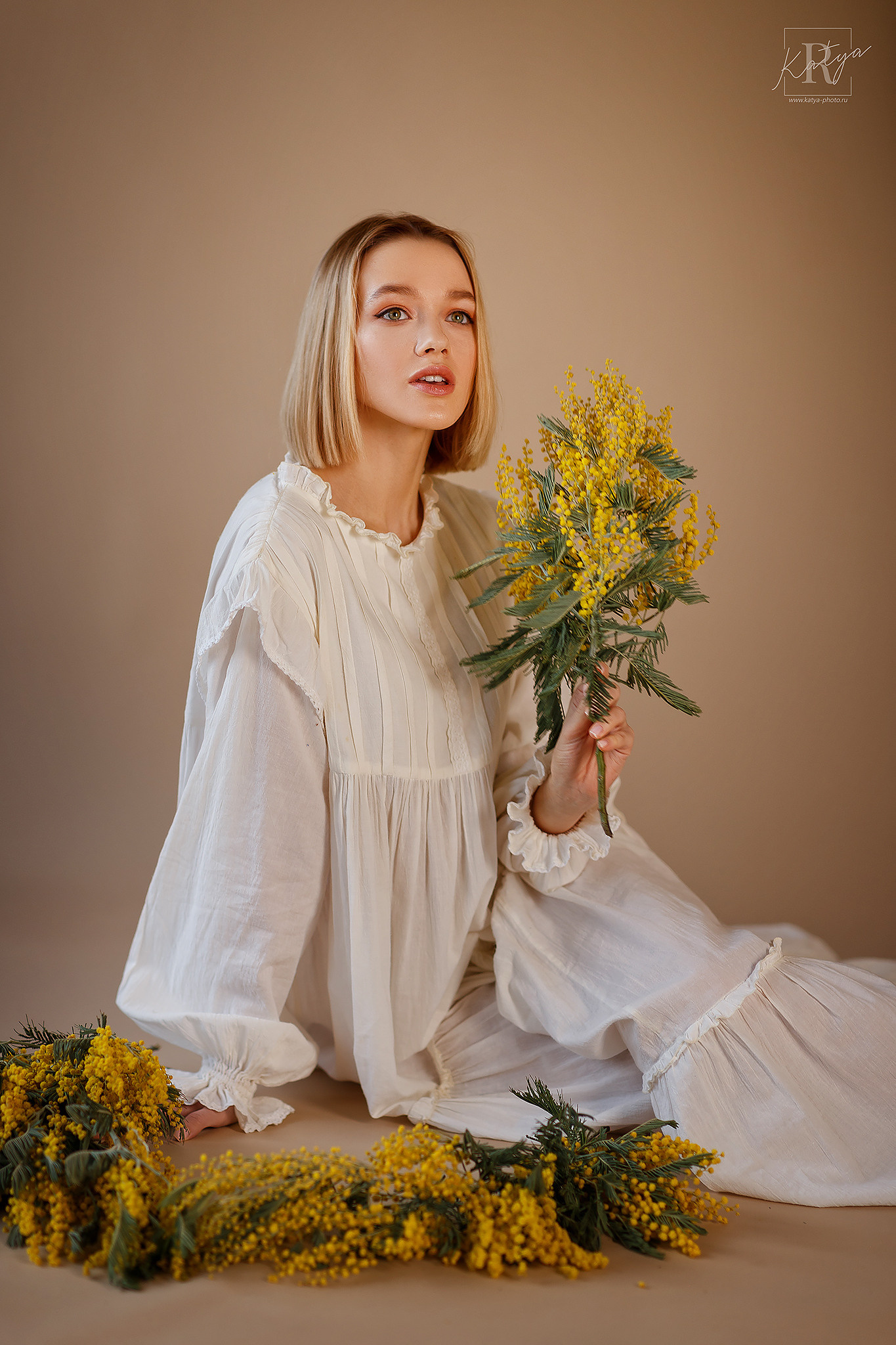 девушка в белом платье с мимозами на бежевом фоне