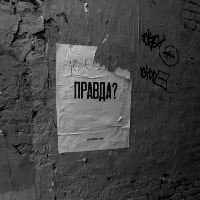 Черно-белая фотография, плакат с надписью "ПРАВДА?" на облупленной кирпичной стене. Проект "Манифест теней" Вадима Топорёнка. Городские шрамы, память и поиск истины в урбанистическом пространстве. Урбанистическая фотография, городская философия, тени памяти.