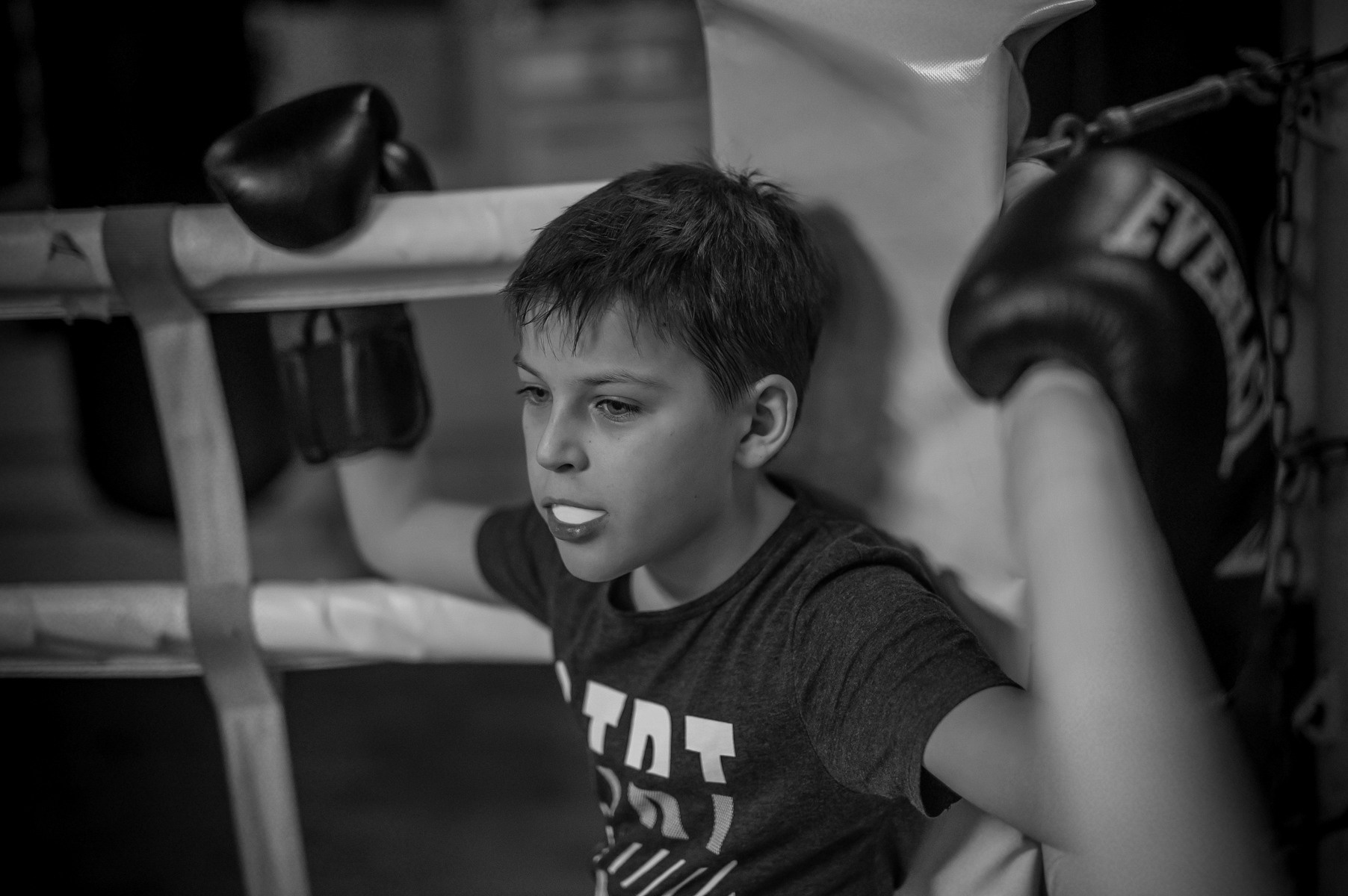 Мальчик отдыхает в углу ринга в боксерских перчатках, белая капа во рту