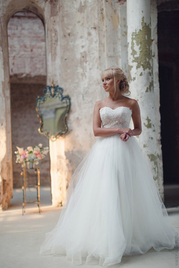 Невеста смотрит на своего жениха, когда они проходят под аркой из цветов, освещенной мягким солнечным светом