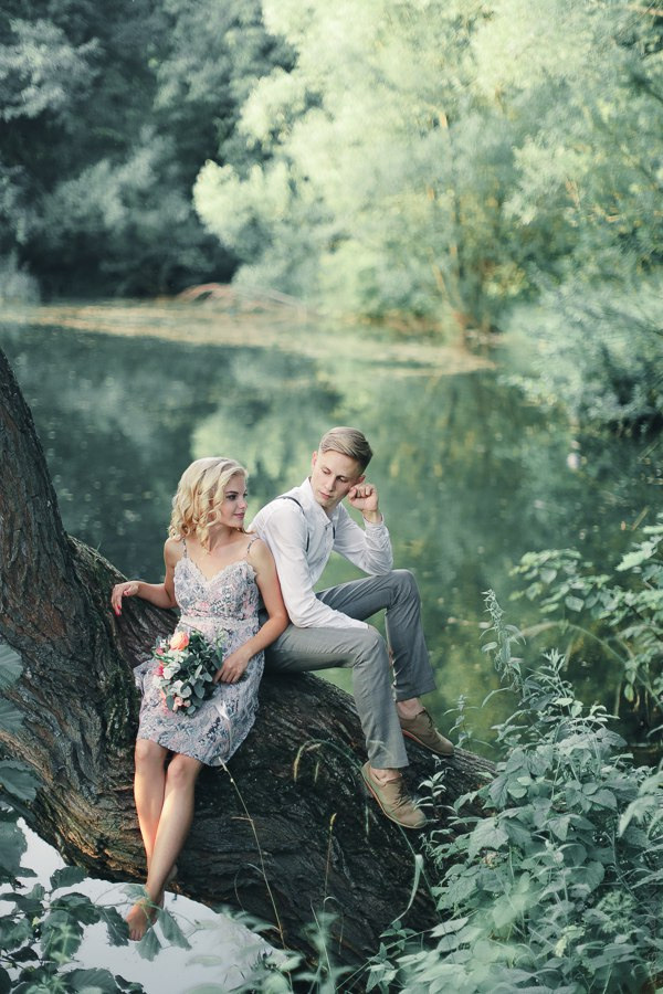 Невеста прижимает руку жениха к своему сердцу на фоне весеннего парка, полного цветов и молодой зелени, что создает ощущение обновления и возрождения