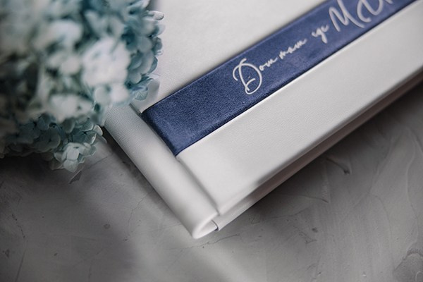 Крупный план тактильной синей ленты с серебристым тиснением текста на фоне идеально белой кожи обложки.