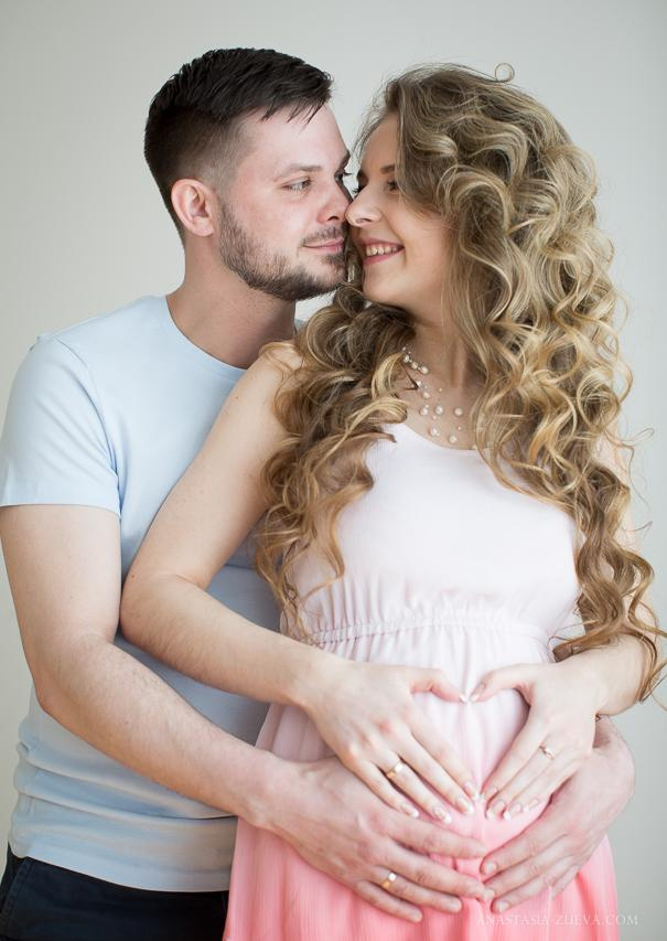  Влюбленная пара с нежностью смотрит друг на друга, из их рук сложено сердечко на животе беременной девушки