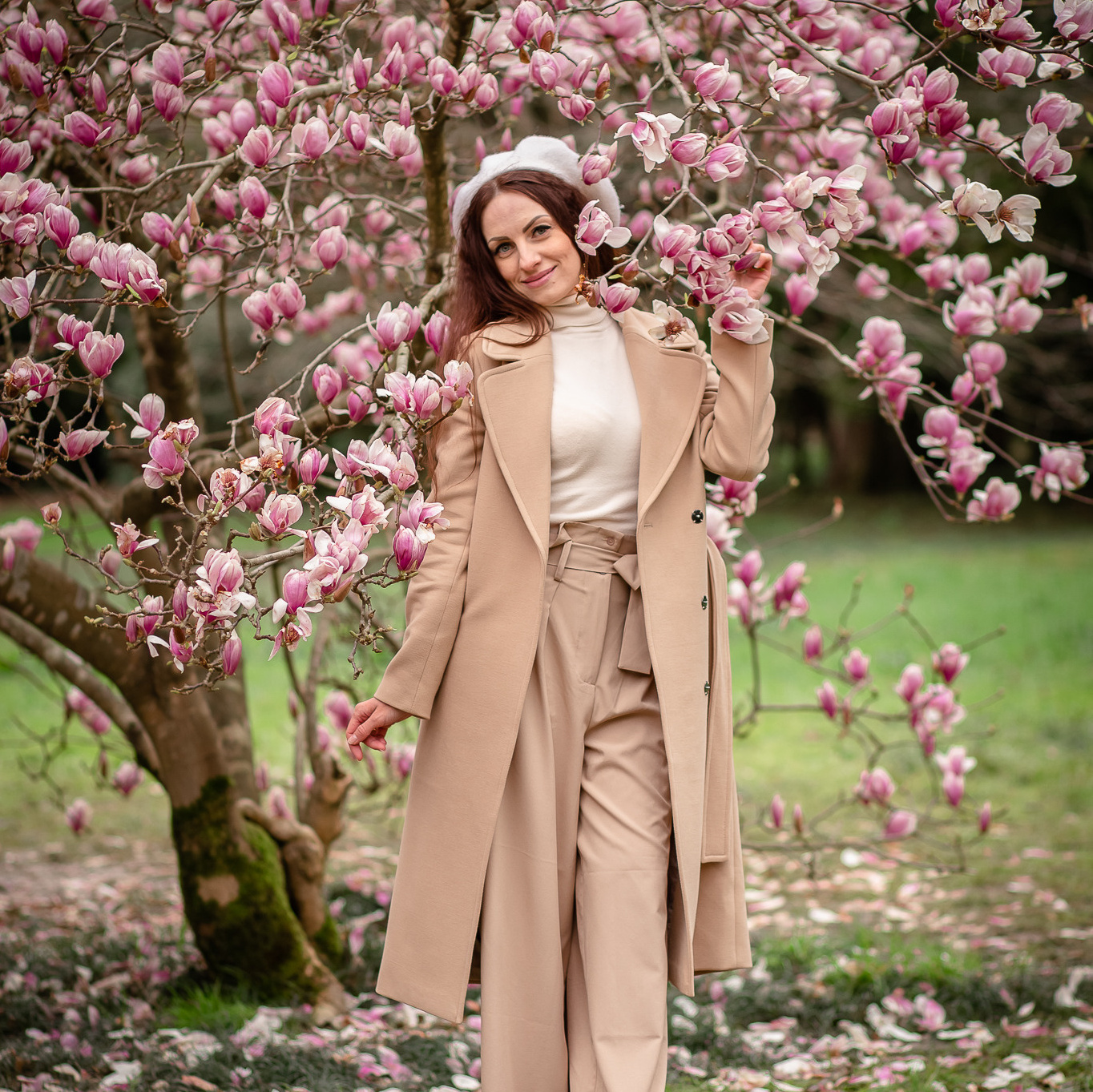 Молодая женщина в бежевом пальто на фоне дерева Магнолии и множество цветов