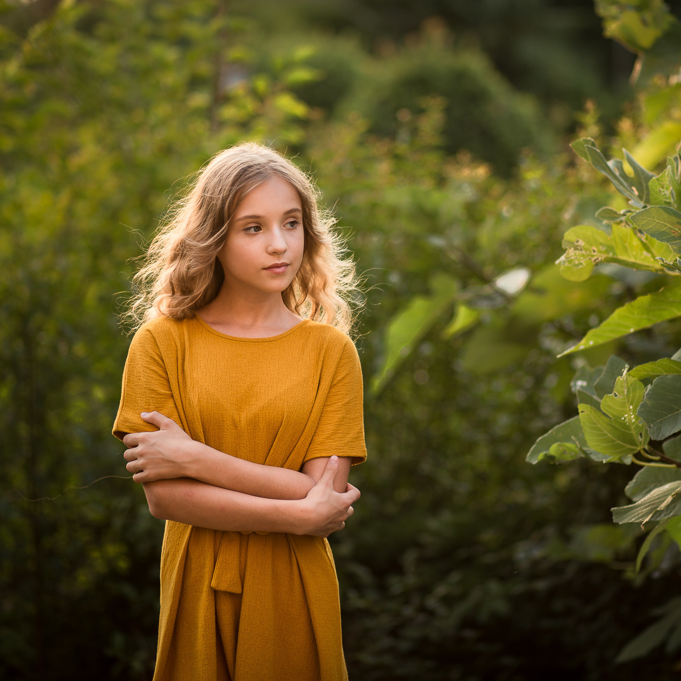 Девочка подросток с русыми волосами на фоне зеленного куста инжира