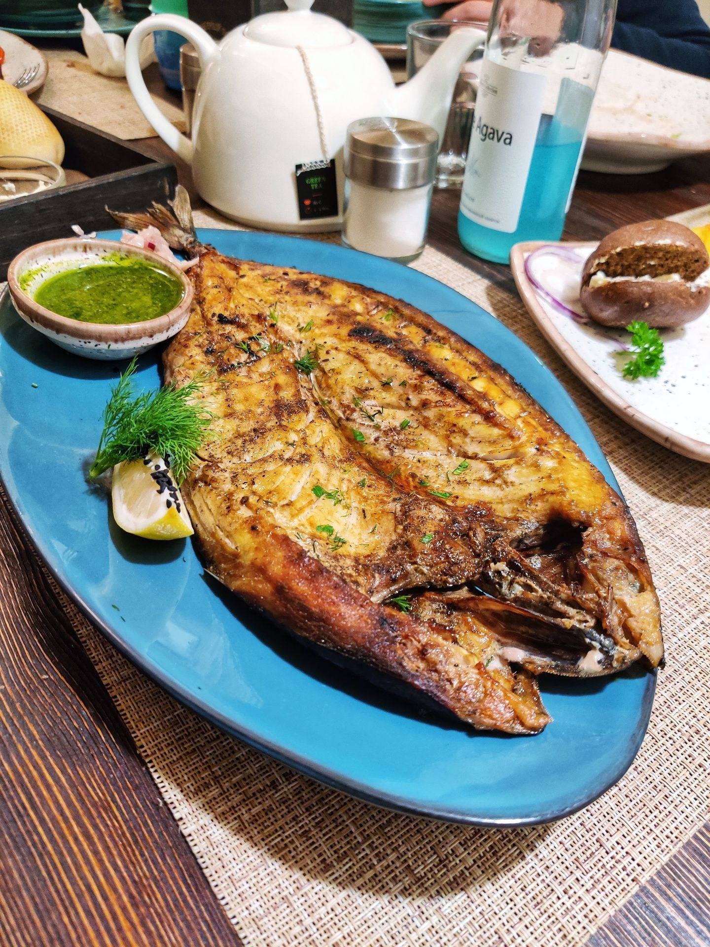 Запечённая рыба на синем блюде с лимоном, зеленью и соусом на столе в ресторане