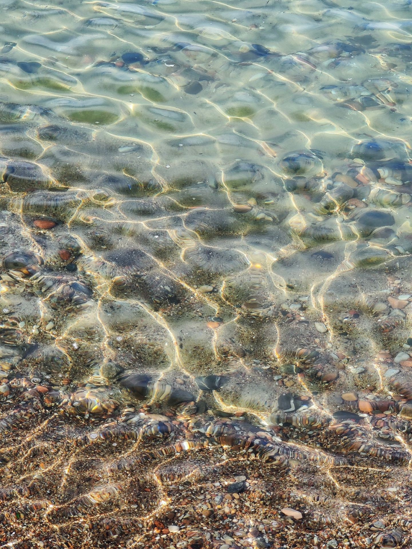 Чистая морская вода с игрой солнечных бликов на поверхности и разноцветной галькой на дне у берега