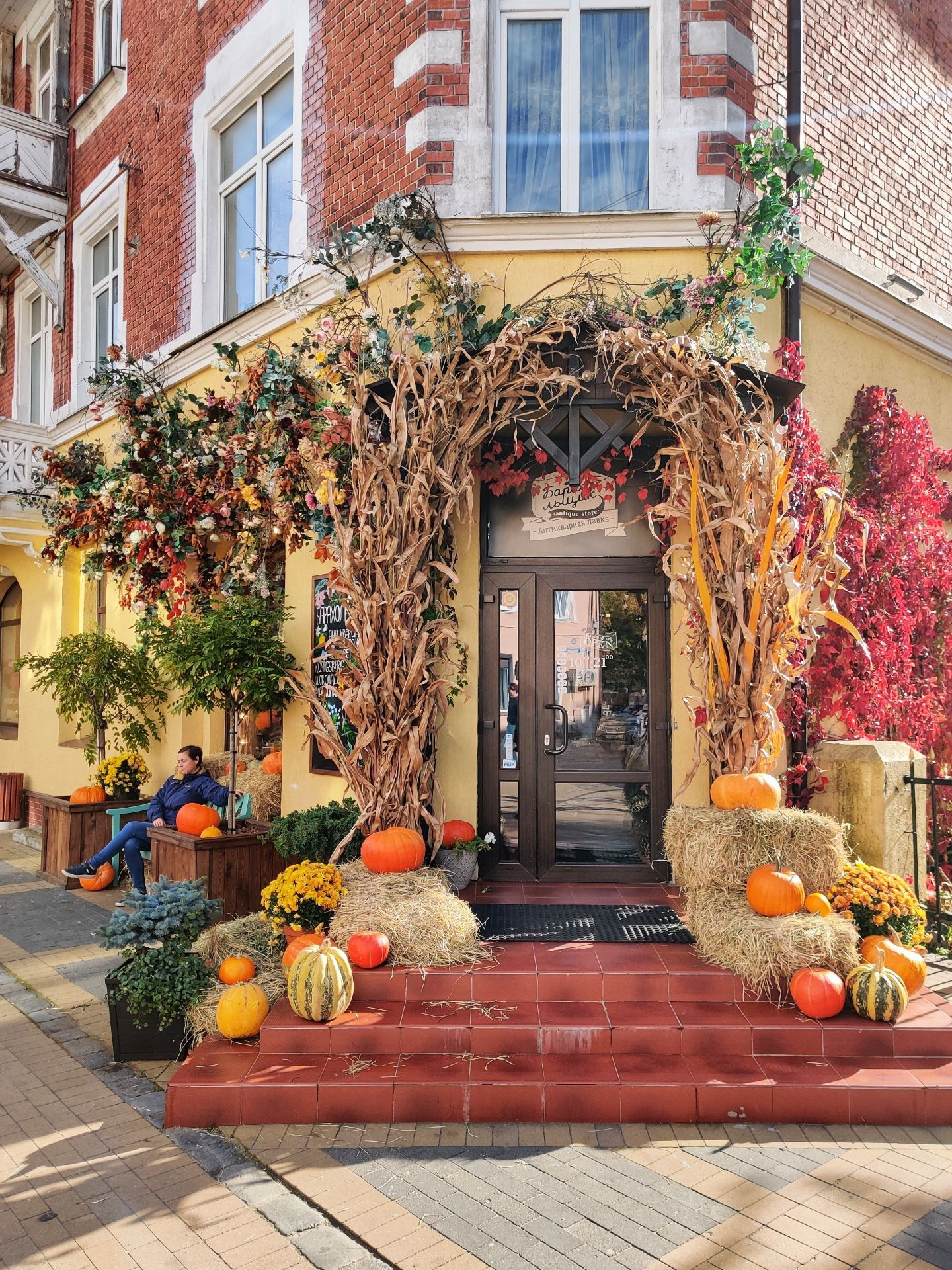 Осенний декор у входа в кафе с тыквами, соломой и цветами, создающий атмосферу уюта и праздника
