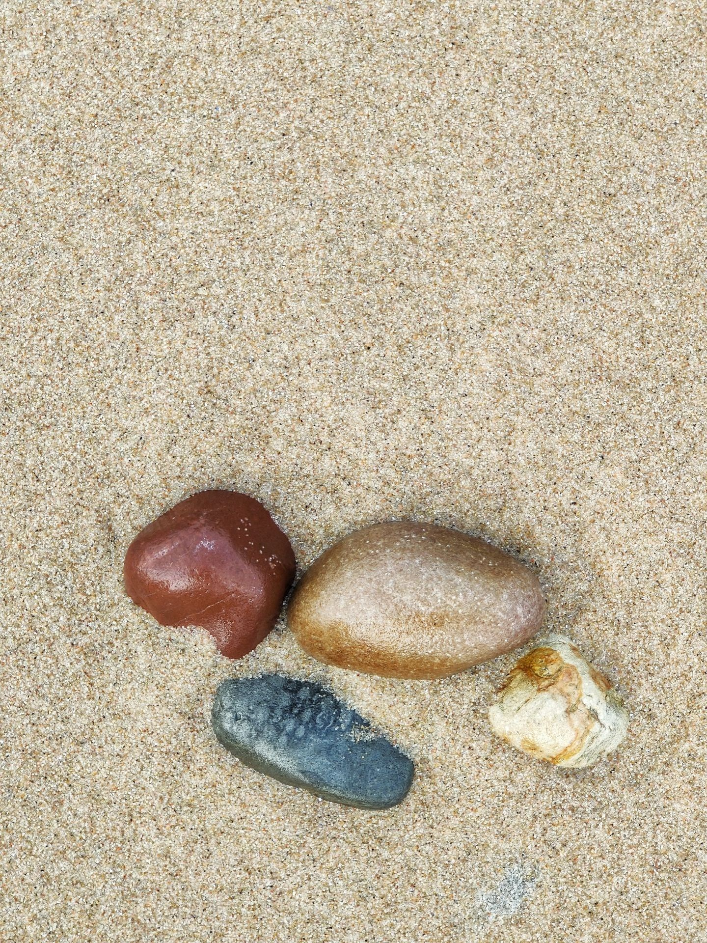 Четыре разноцветных камня лежат на песчаном пляже