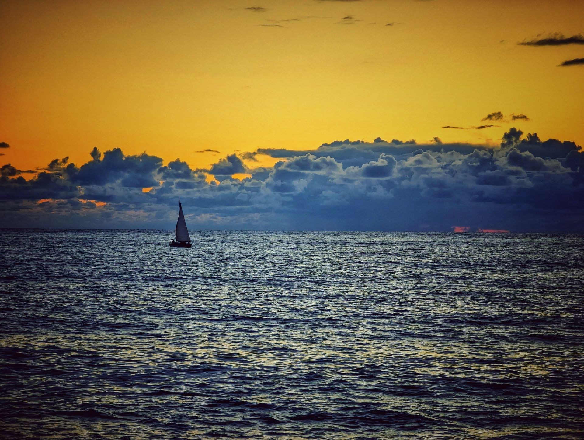 Парусник на фоне заката, спокойное море и облака создают атмосферу умиротворения