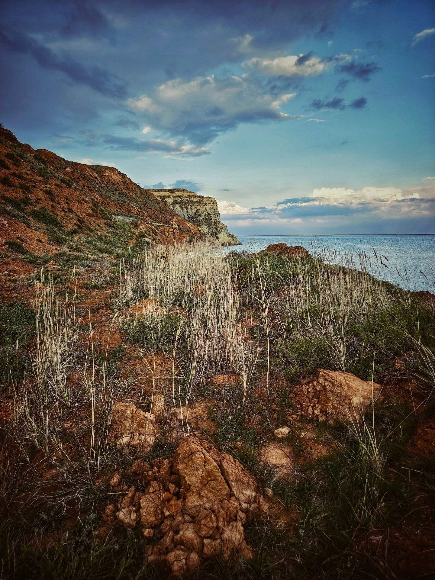 Скалистый берег, река, небо с облаками и сухая трава