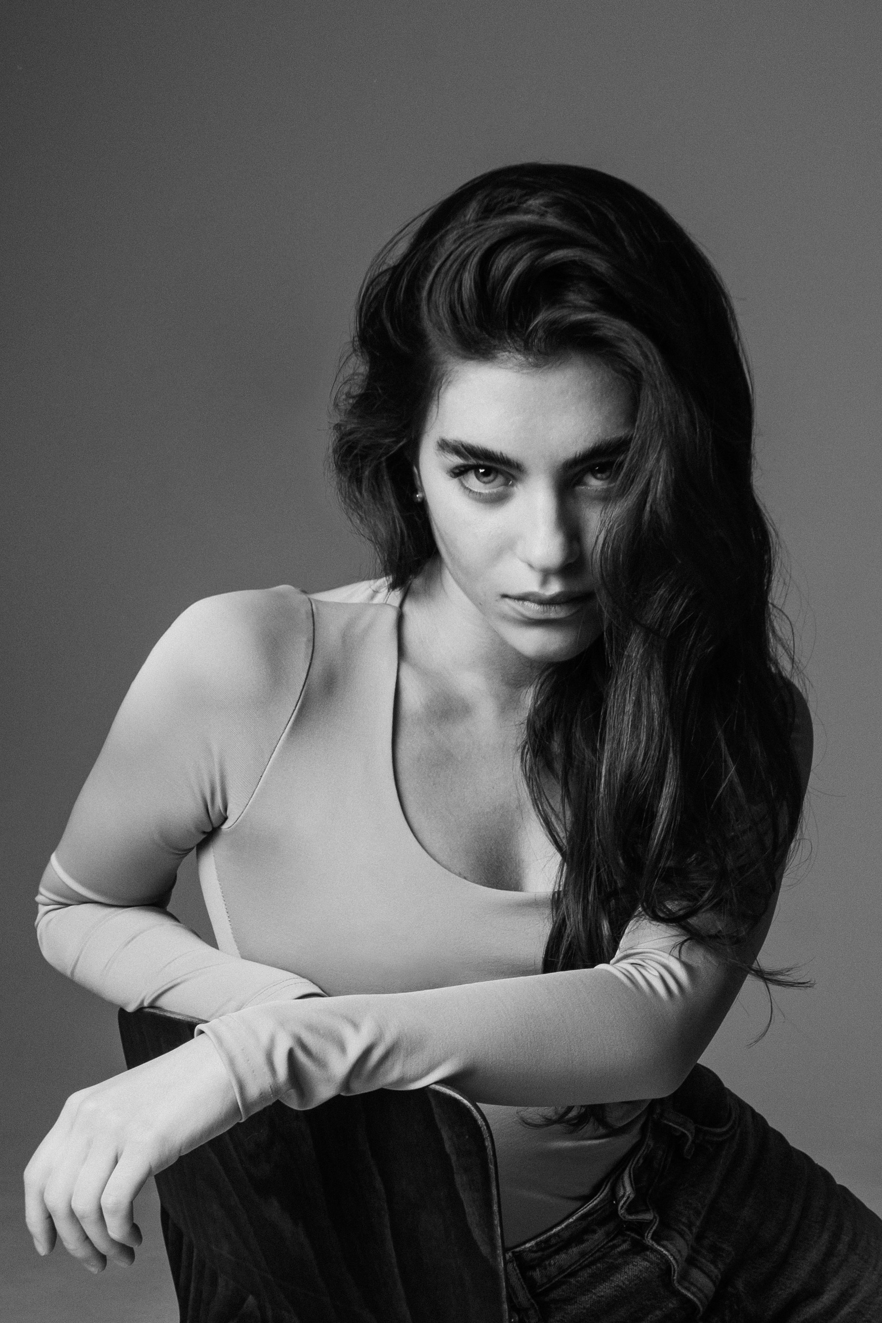 Черно-белый студийный портрет грузинской модели. Девушка сидит, облокотившись на спинку стула, и смотрит на нас исподлобья