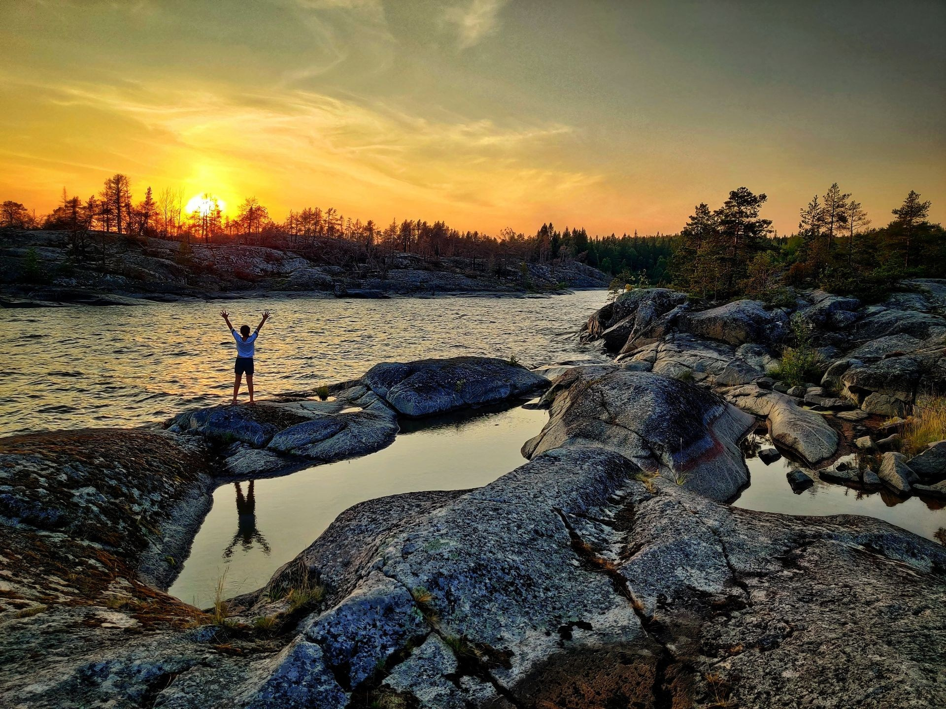 Девочка, стоящая на скале у воды на фоне заката