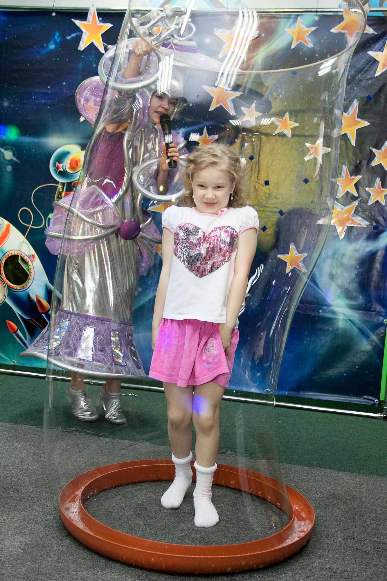 Девочка в белой футболке и розовой юбке стоит в мыльном пузыре.