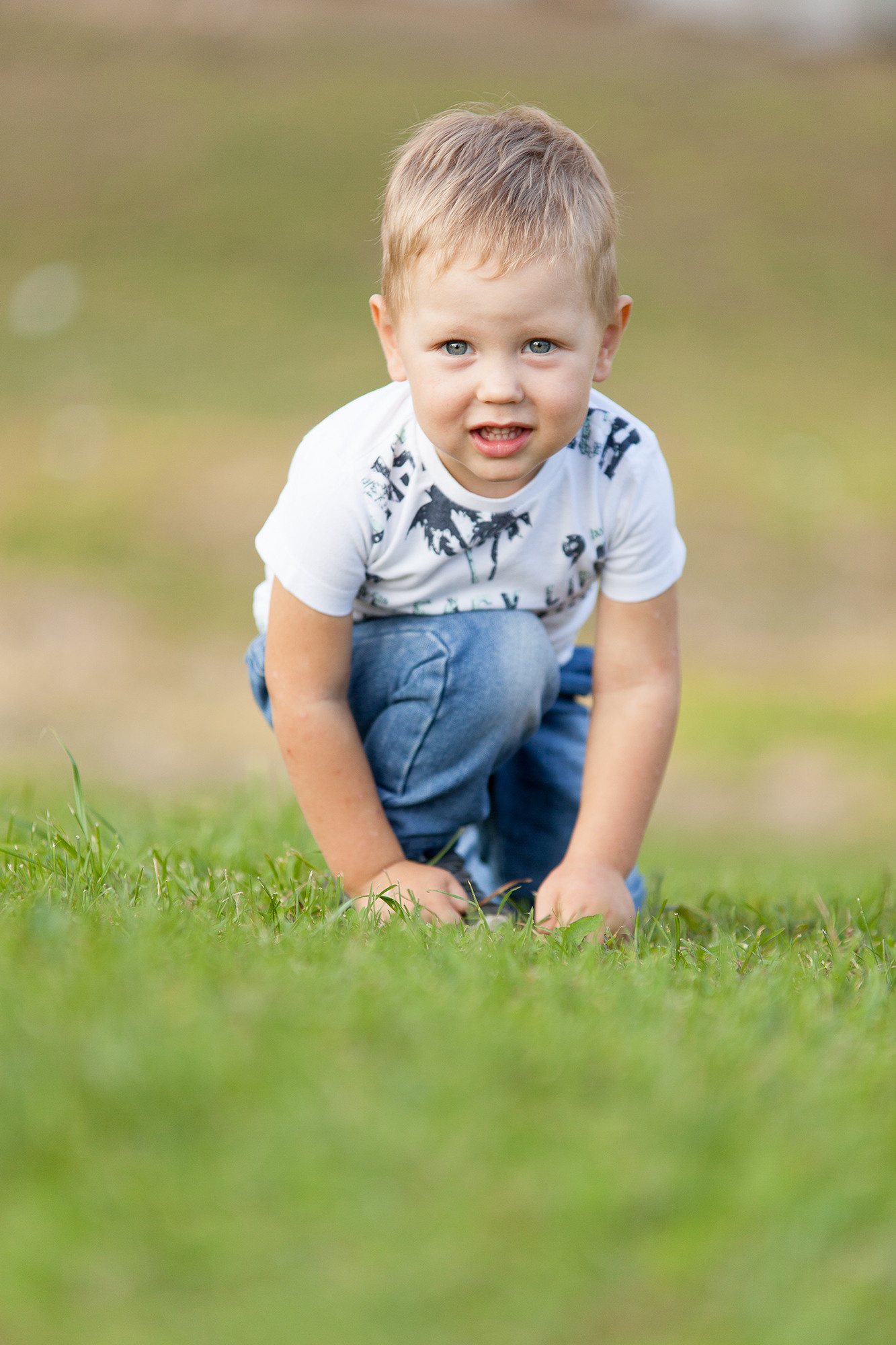 Мальчик в белой футболке и джинсах поднимается по зеленому склону.