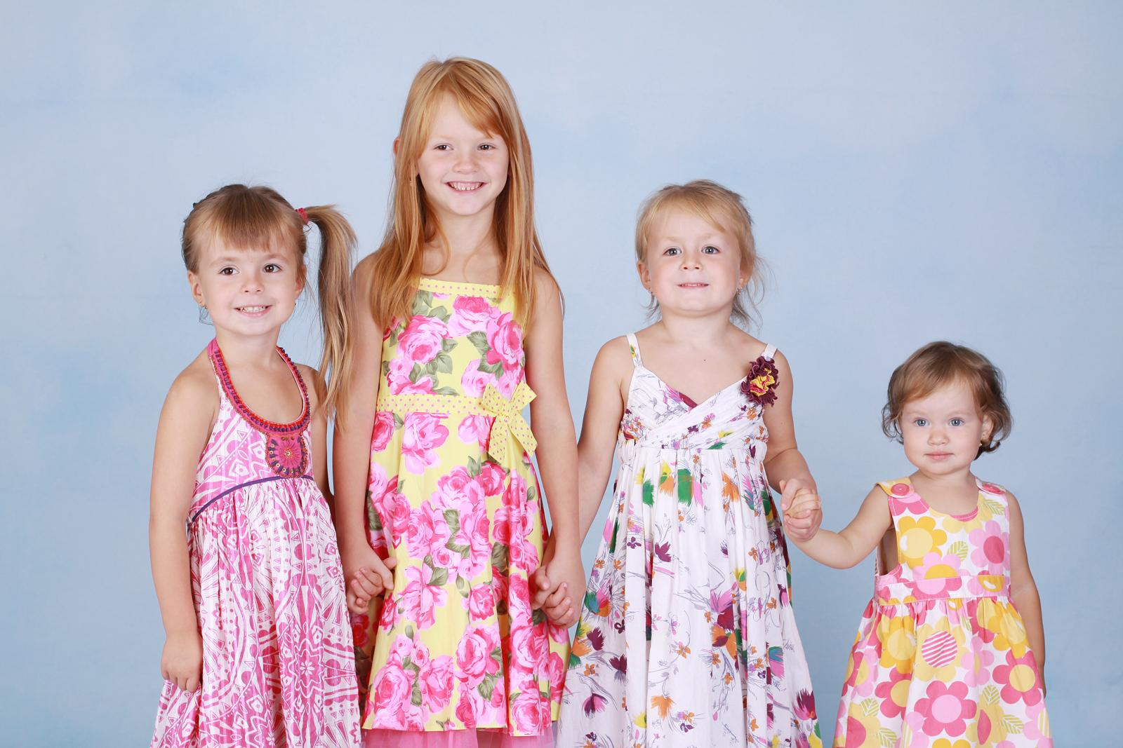 Четыре девочки стоят на фоне голубого фона в фотостудии.