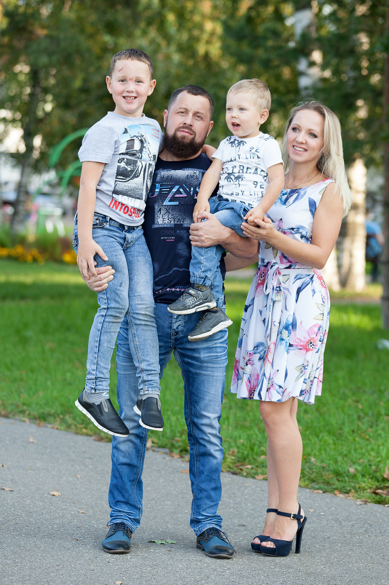 Папа, мама стоят на тротуаре и держат на руках двух сыновей.