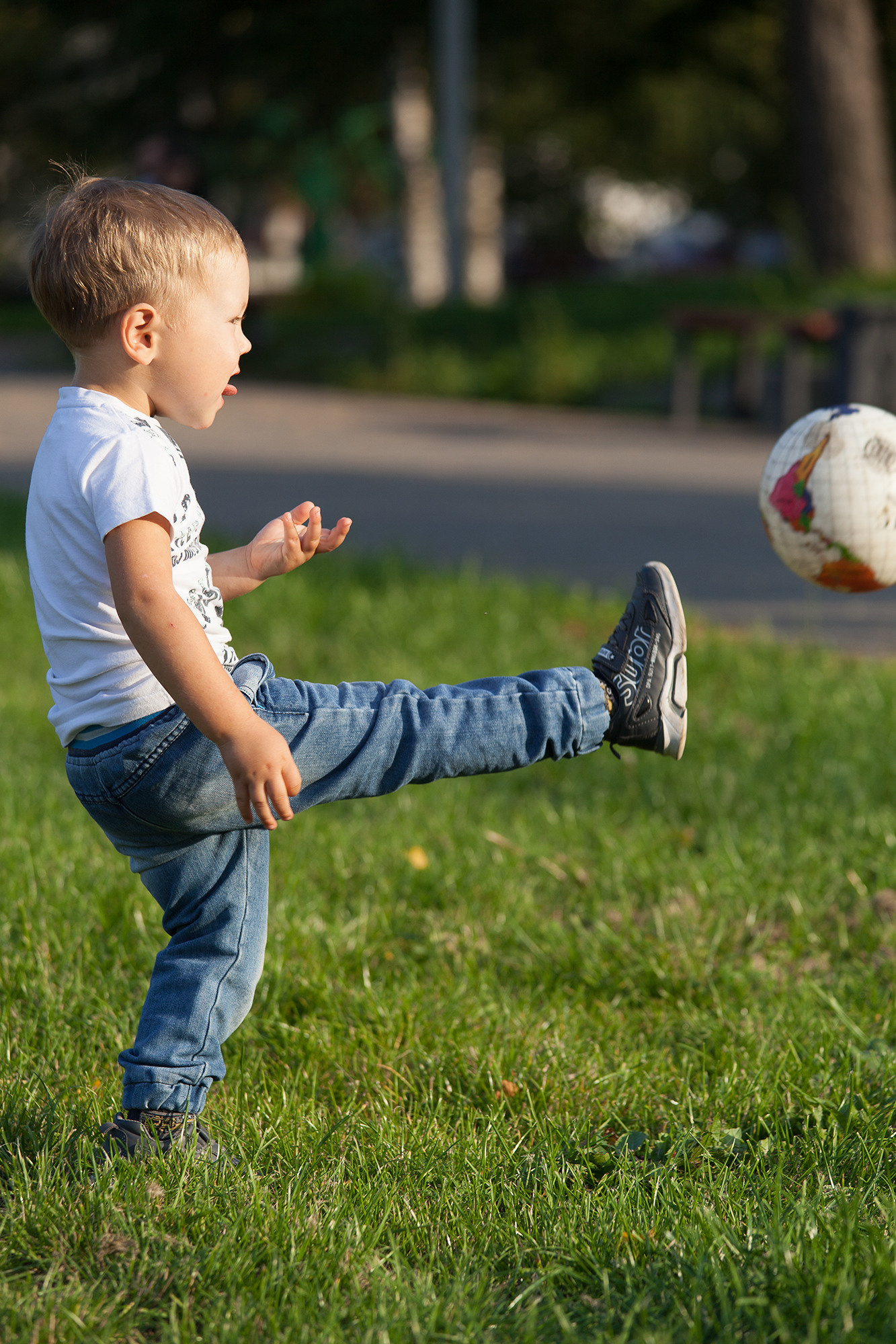 Мальчик в джинсах и футболке пинает мяч.