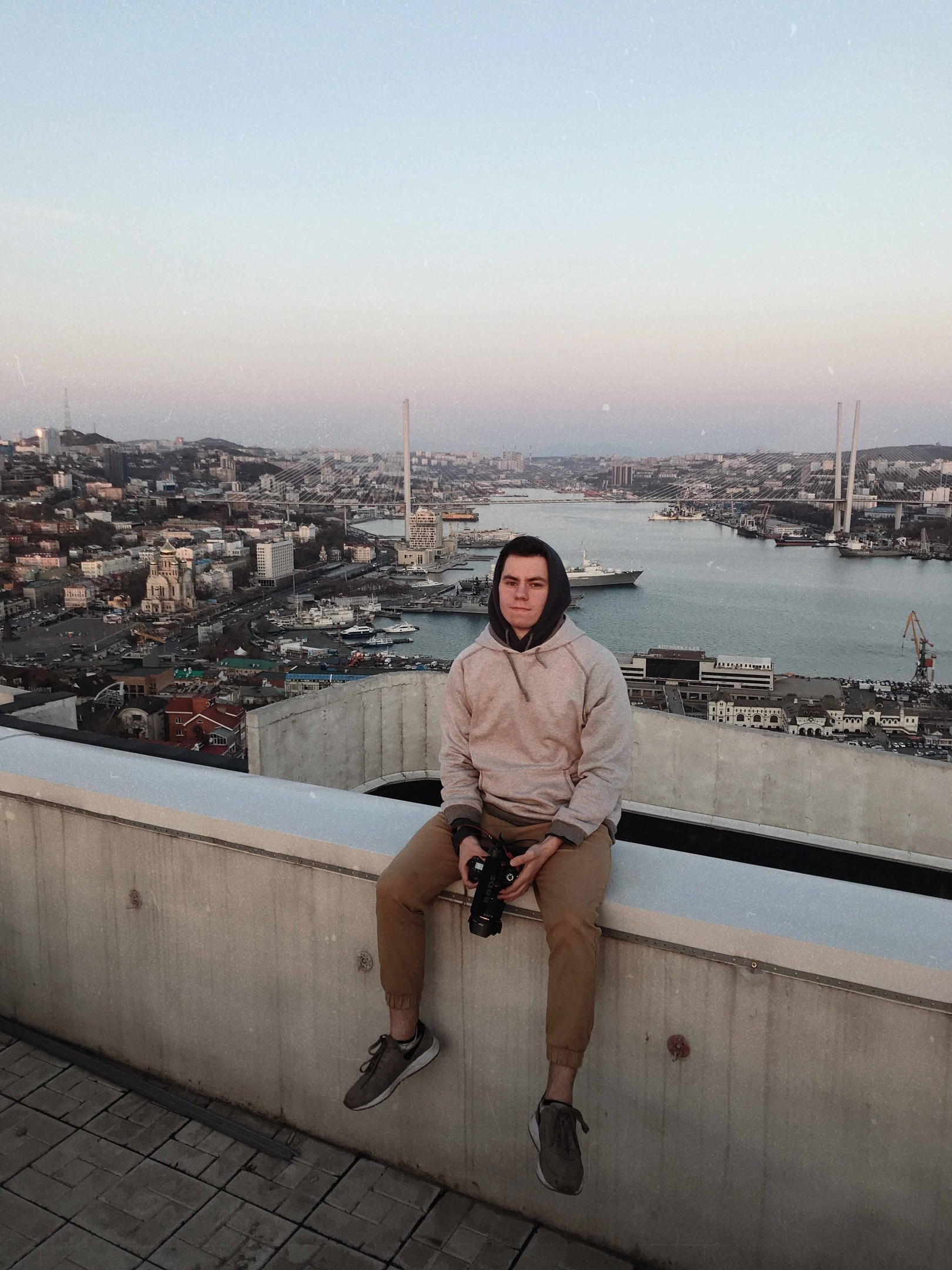 Мужчина сидит на крыше с видом на Владивосток и Золотой мост