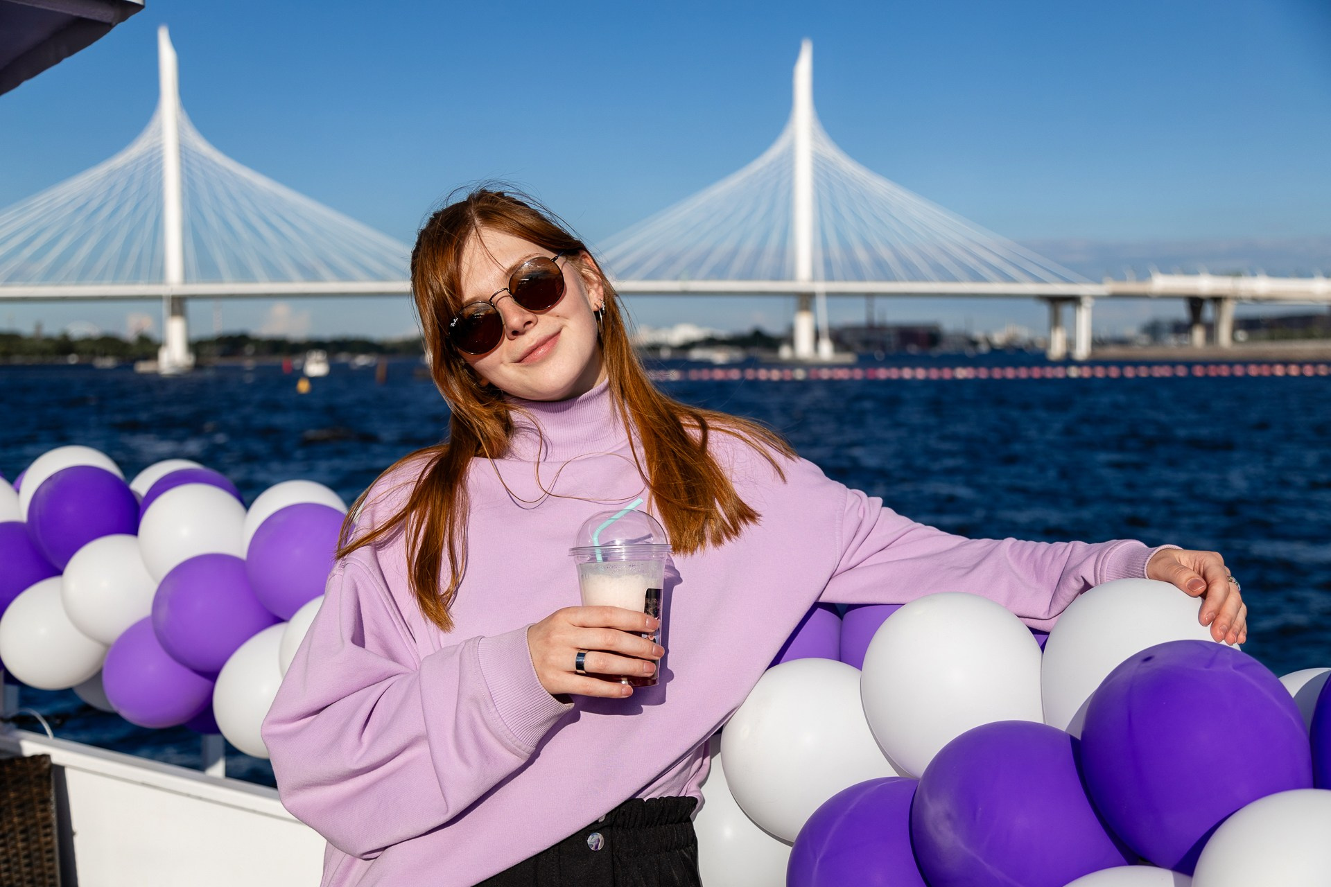 Фото красивой девушки с коктейлем в руке на теплоходе на фоне Вантового моста в Санкт-Петербурге