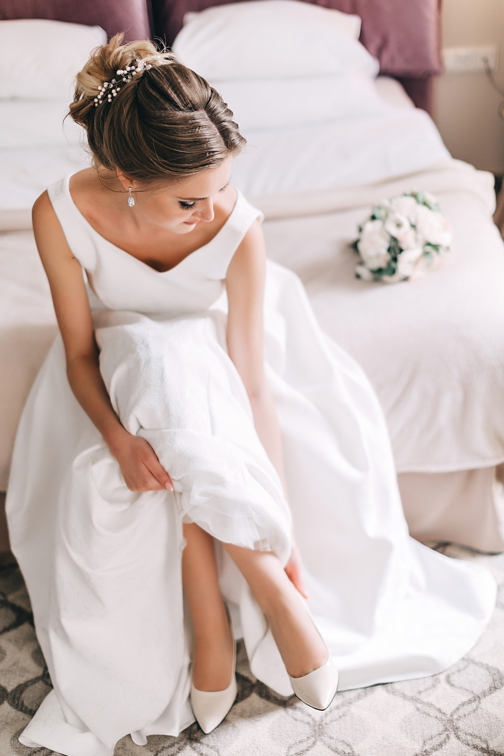 Невеста надевает свадебные туфли в номере отеля