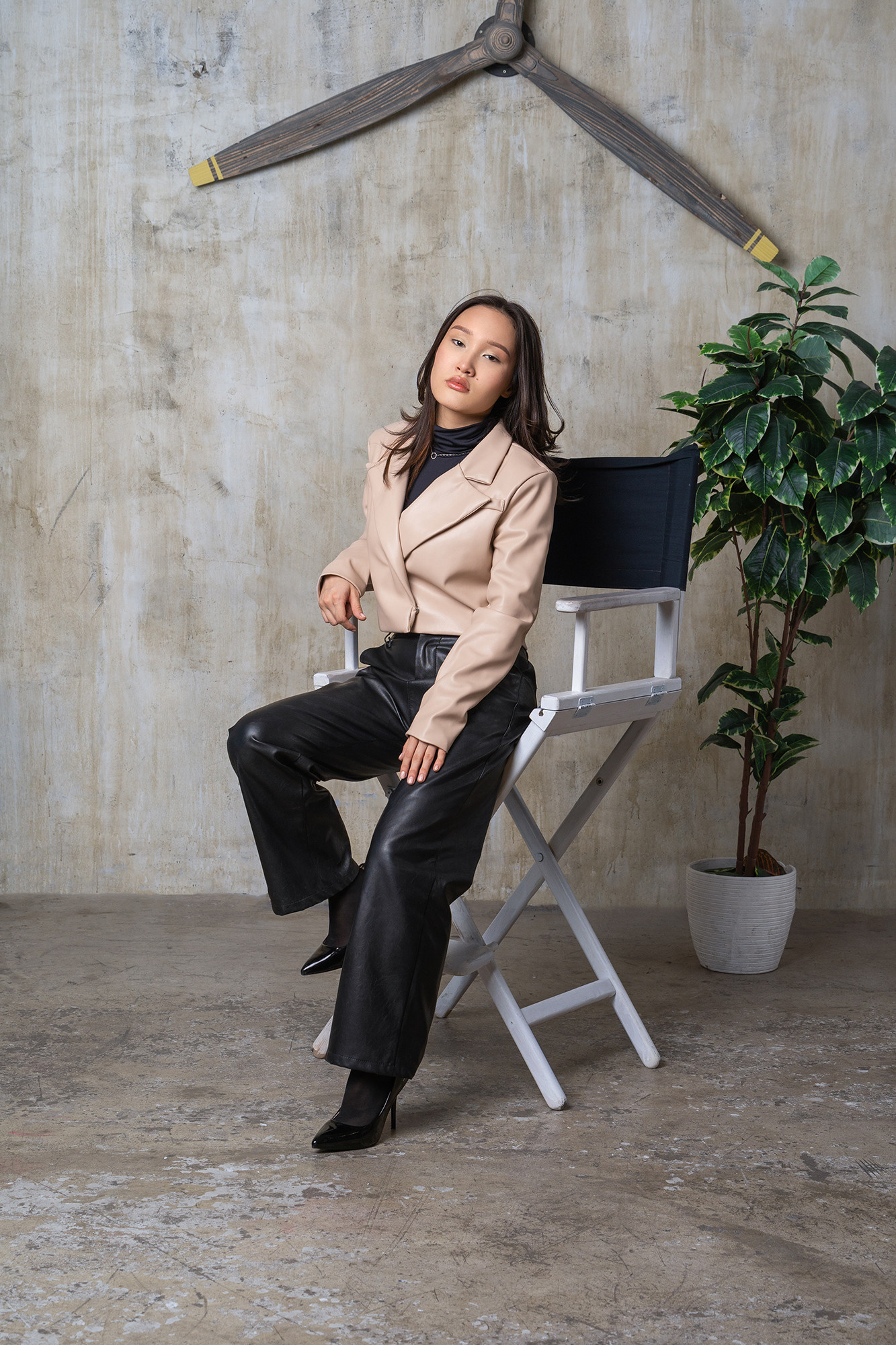 Девушка-казашка в черных кожаных брюках облокотилась на высокий стул.