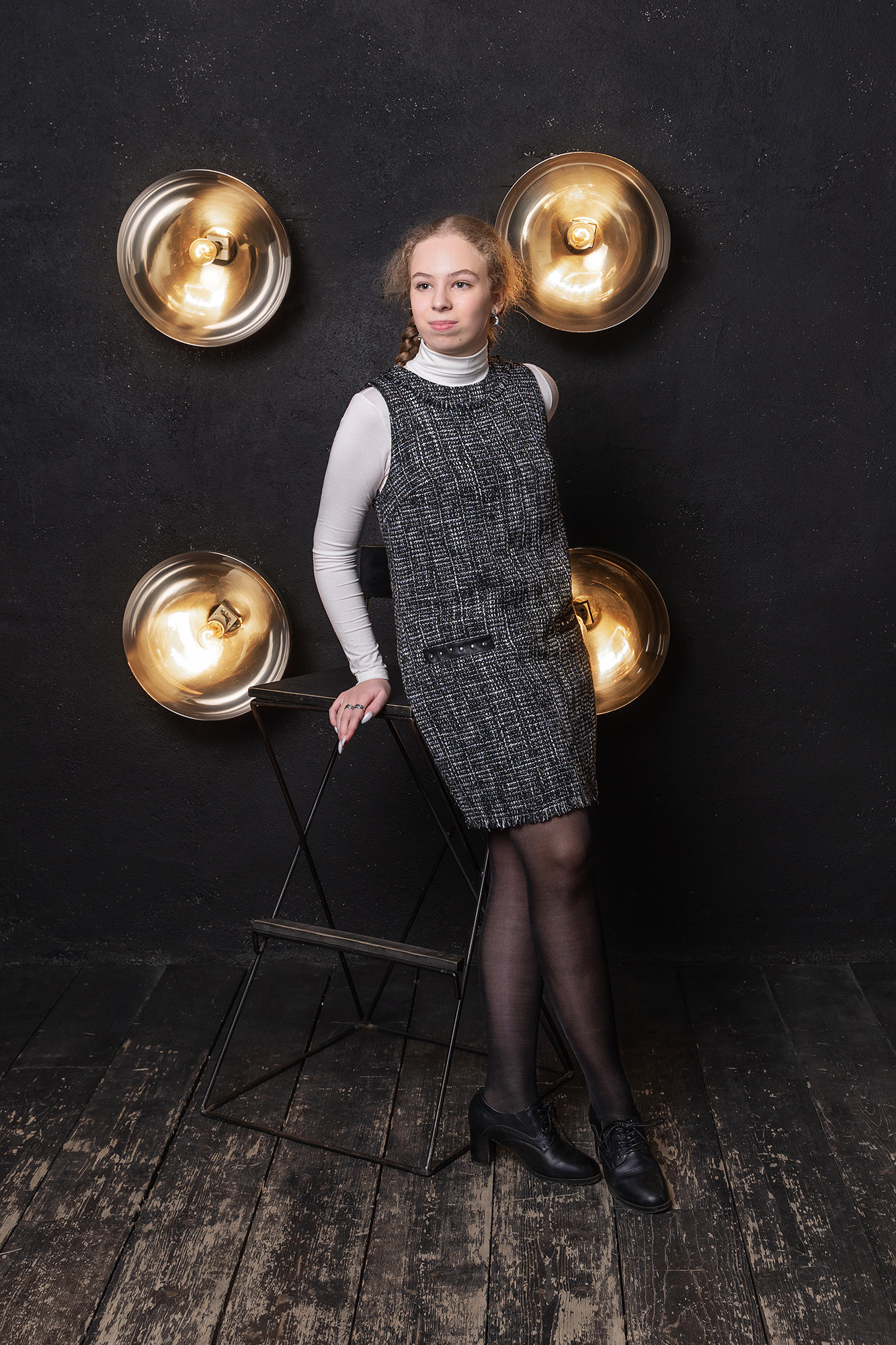 Девушка стоит на фоне черной стены с четырьмя встроенными лампами-прожекторами.