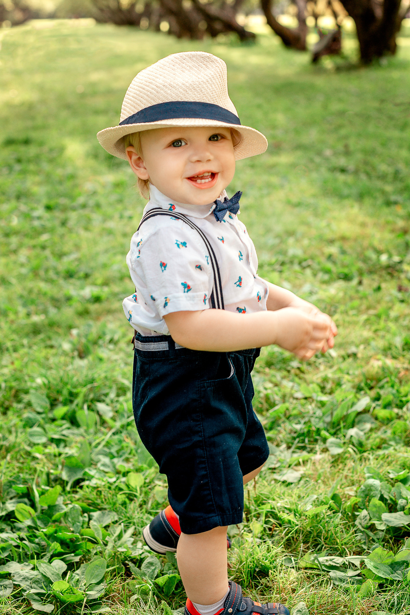 Малыш в шортиках, с бантиком и шляпкой улыбается и убегает.