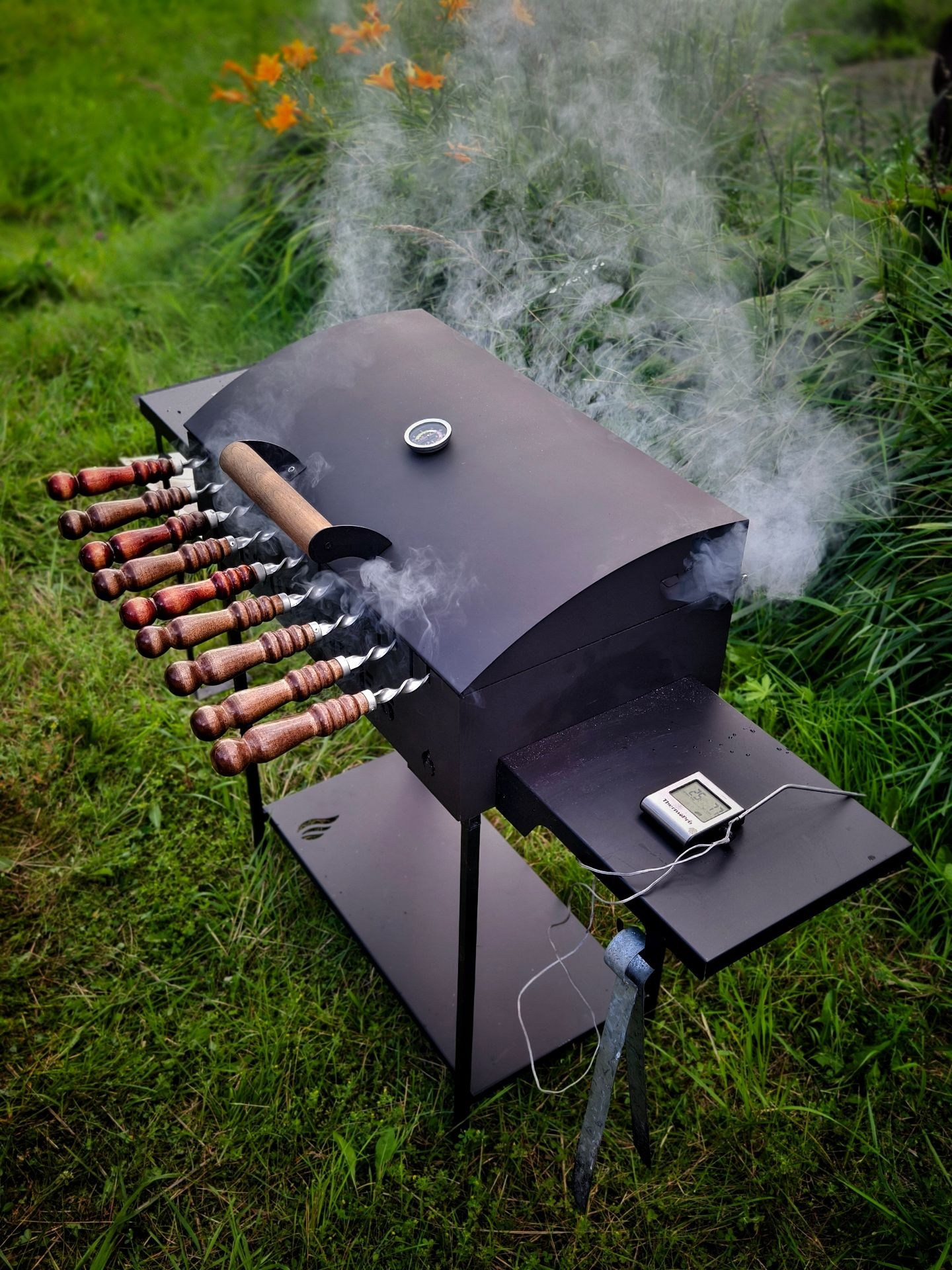Мангал с коптильней и термометром на природе, окружённый газоном