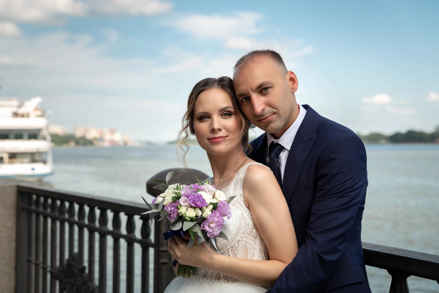 Жених обнимает невесту с букетом на набережной