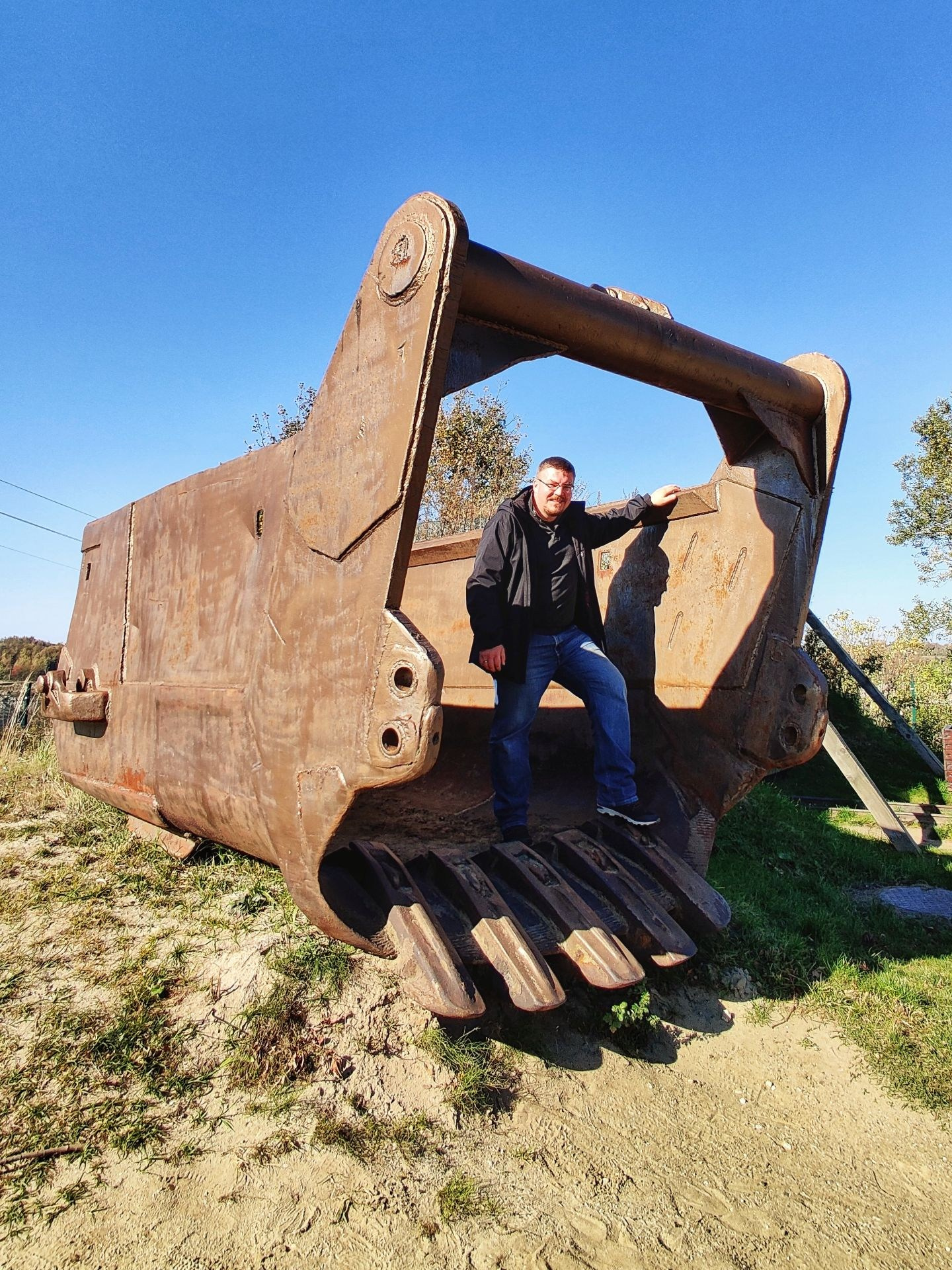 Человек стоит внутри огромного ковша экскаватора на фоне голубого неба