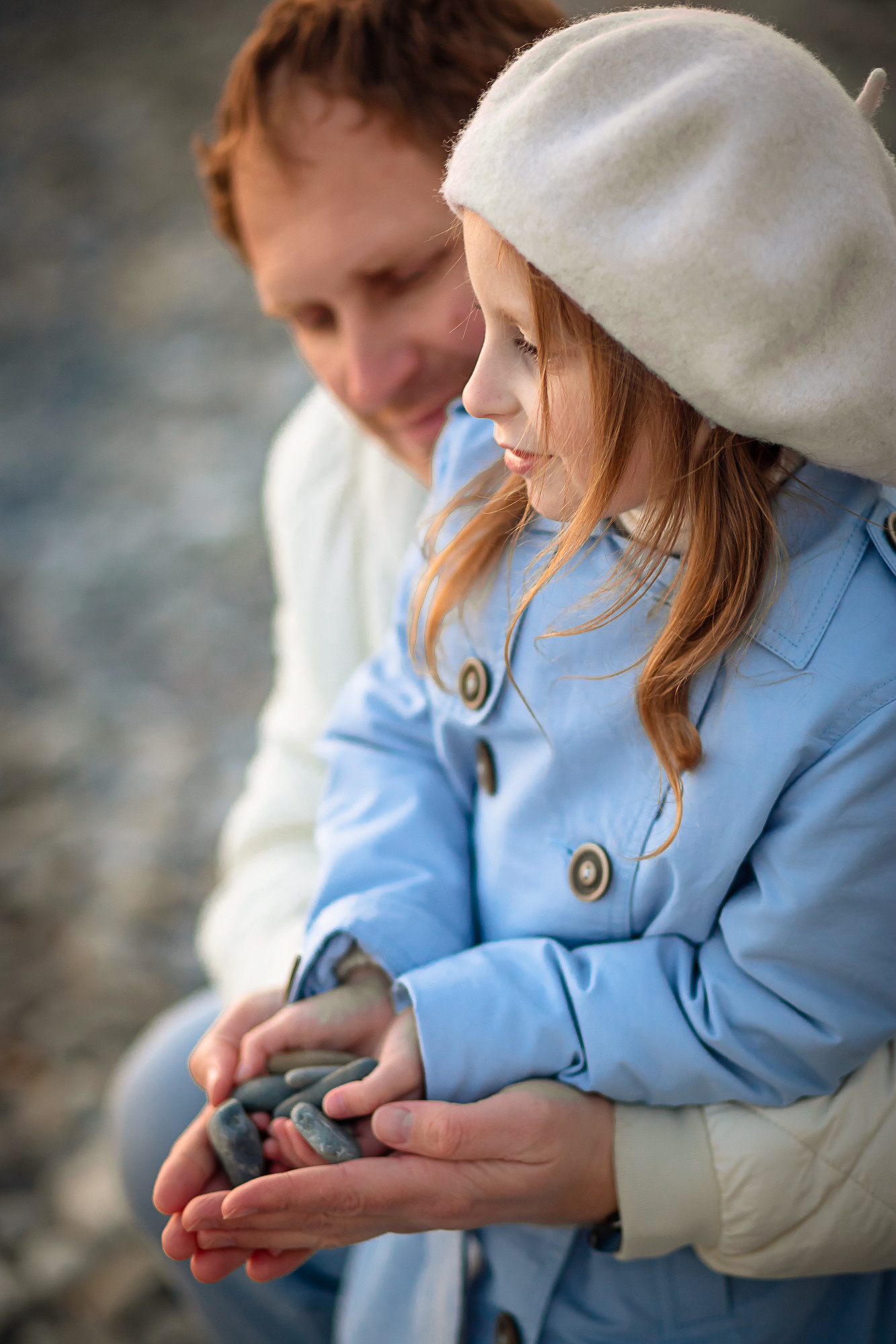 Девочка в голубом тренче на пляже с папой на фоне морских камней 