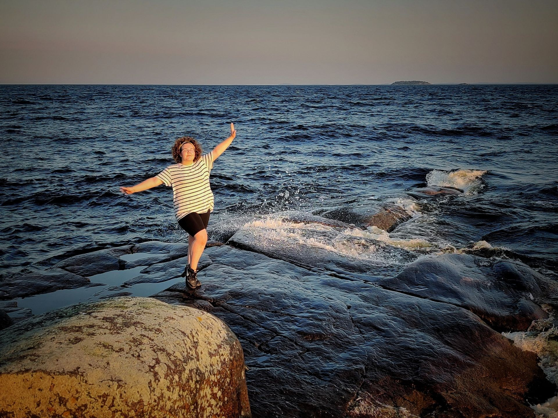 Девушка с раскинутыми руками стоит на скале у моря, наслаждаясь свободой