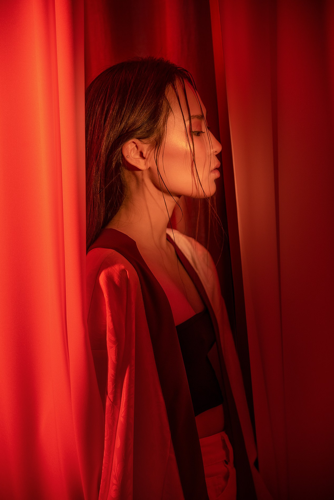 Девушка азиатской внешности в красном на фоне тканей.