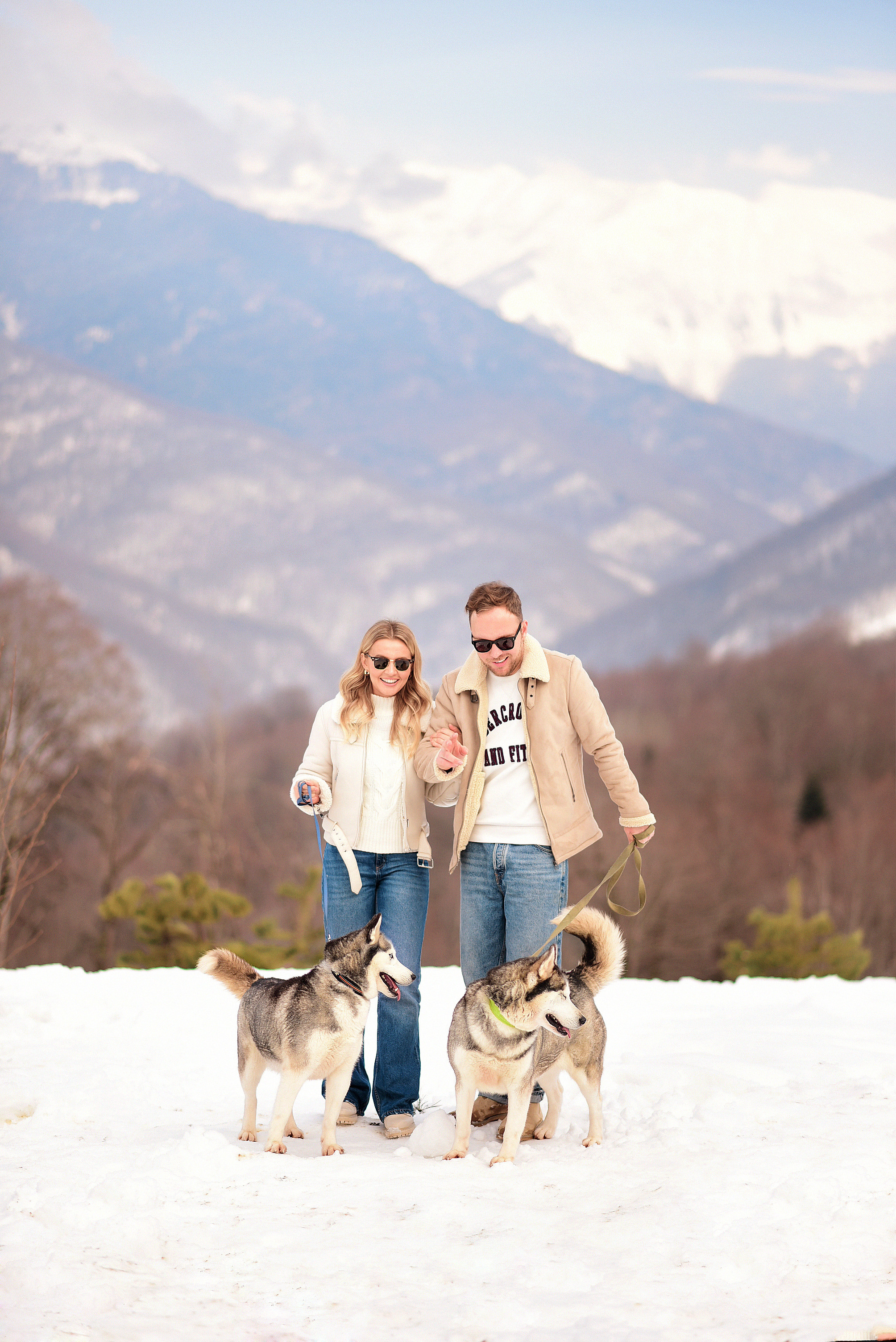 Девушка с парнем гуляют с хаски в заснеженных горах Сочи.